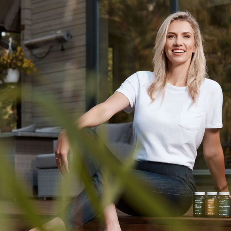 A woman seated outdoors beside a small selection of Ecosh bottles.