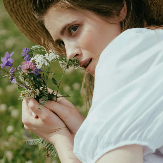 A woman holding wildflowers in a sunlit garden.